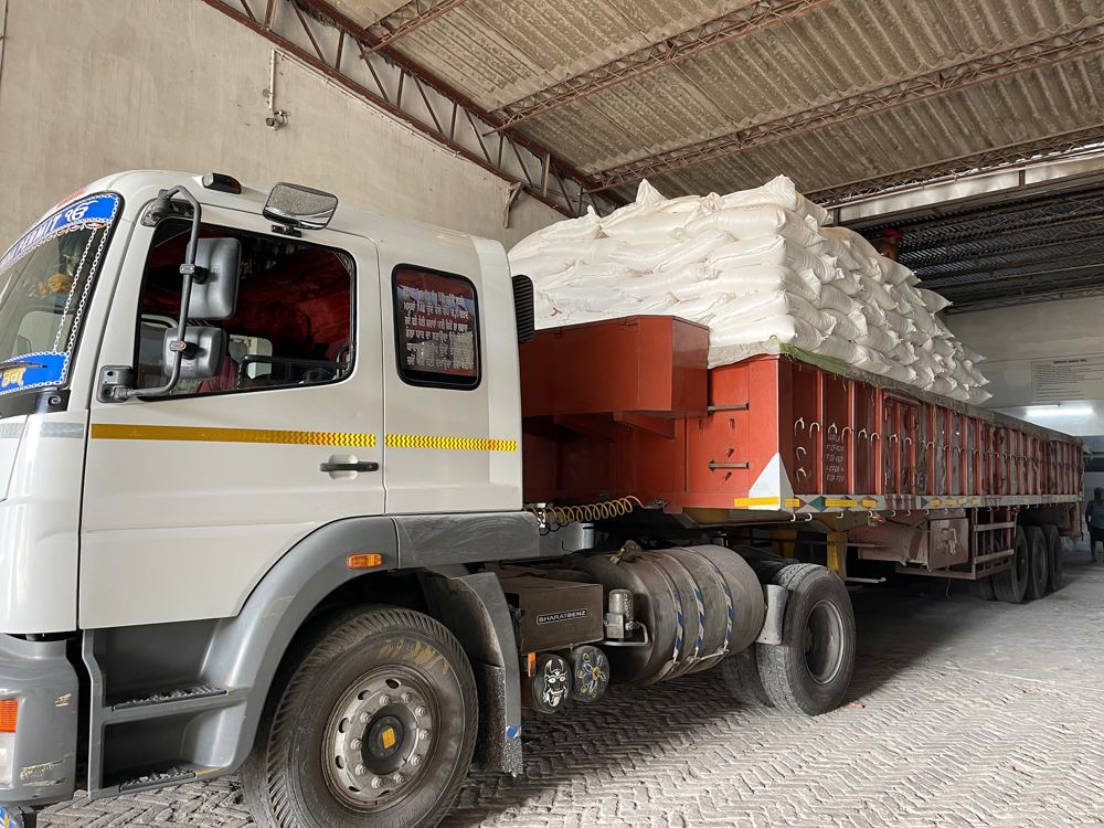 A trailer truck loaded high with white flour sacks inside a loading shed