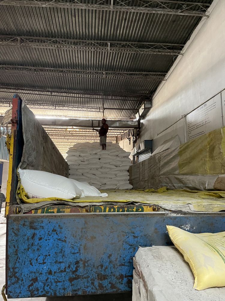 Workers moving flour sacks from a trailer inside a covered shed