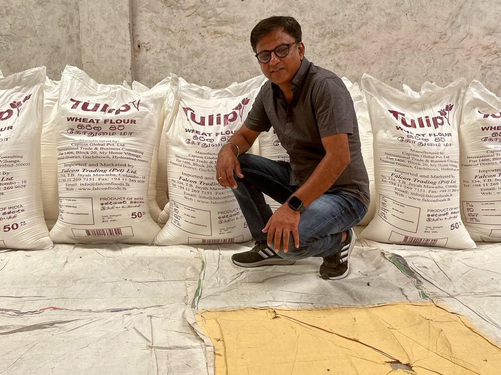 A man in a grey polo shirt crouching in front of a row of Tulip wheat flour sacks at the mill