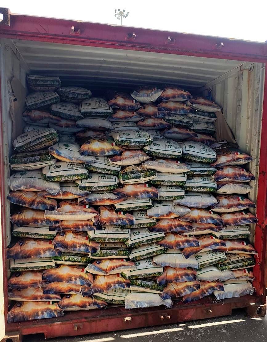 An open red shipping container filled with rice sacks up to the doors
