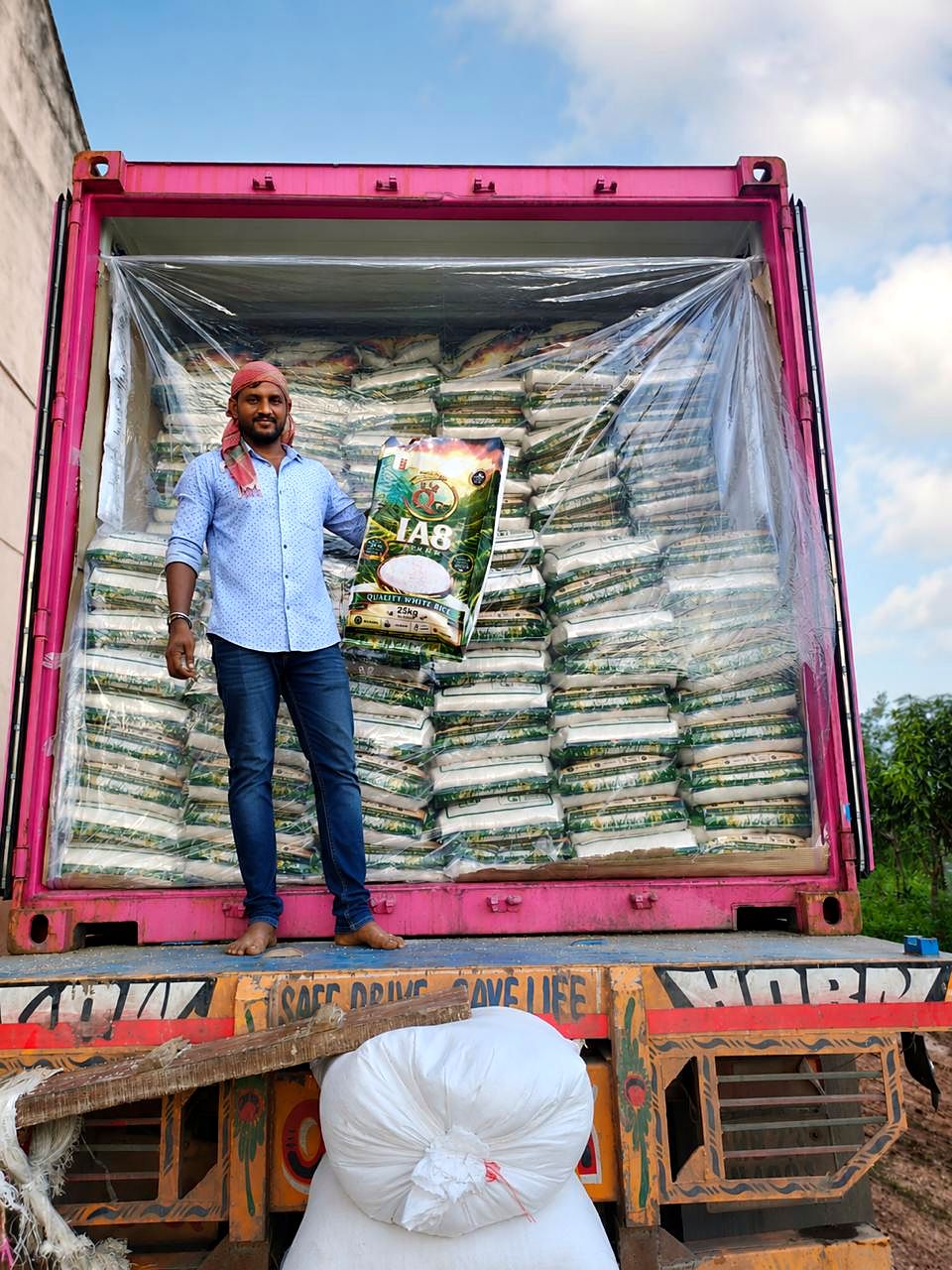 A worker holding up a printed 25 kg rice bag at the door of a container packed with the same bags