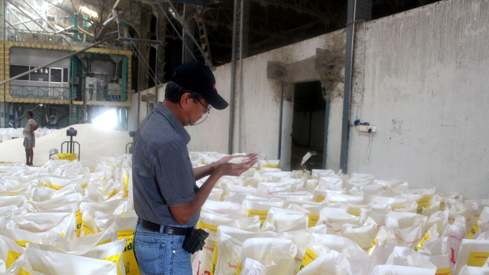 A man checking a handful of rice grains in a mill warehouse full of filled sacks
