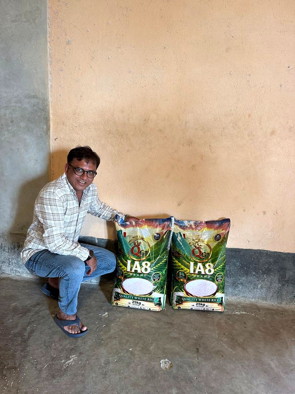 A man sitting beside two printed 25 kg rice bags against a warehouse wall