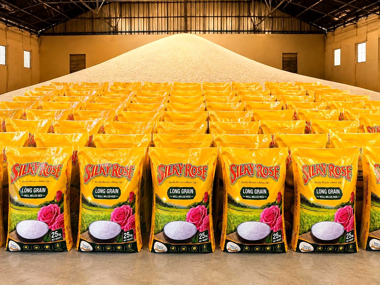 Rows of printed 25 kg long-grain rice bags laid out in front of a heap of milled rice in a warehouse